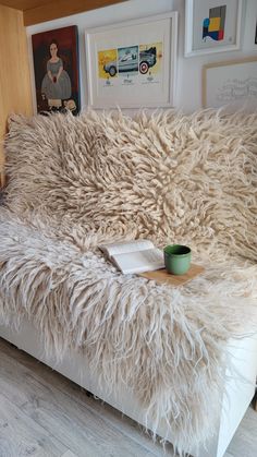 a white couch covered in fluffy fur with a cup on it's end next to pictures