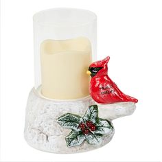 a glass candle holder with a red bird sitting on it's side next to a lit candle