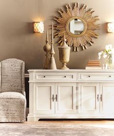 a white dresser topped with lots of drawers under a sun shaped mirror on the wall