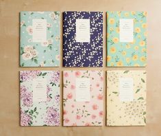 four notebooks are lined up in different colors and patterns, with flowers on them