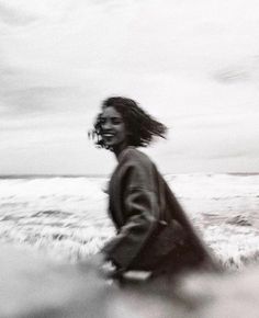 a woman is walking along the beach with her hair blowing in the wind and smiling