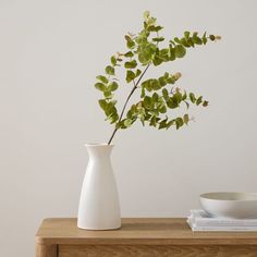 a white vase sitting on top of a wooden table next to a bowl and book