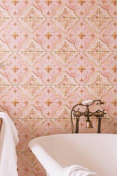 a bath tub sitting next to a white towel on top of a wooden table in front of a pink tiled wall