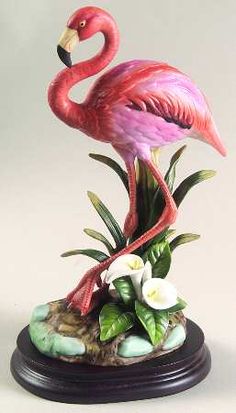 a pink flamingo standing on top of a rock next to some flowers and plants