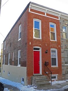 a red door is on the side of a brick building with stairs leading up to it