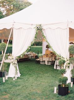 an outdoor tent with tables and chairs set up for a wedding reception in the grass