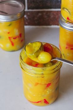 two jars filled with yellow and red pickles on top of a white countertop