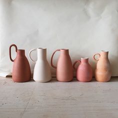 five different colored vases lined up in a row on a white surface next to a pillow