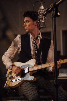 a man with a tie and vest playing an electric guitar in front of a microphone