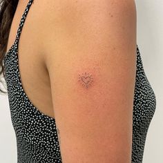 the back of a woman's shoulder with a small sun tattoo on her left arm