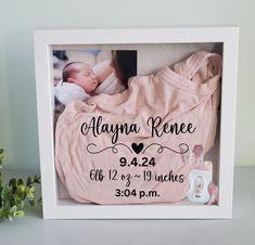 a baby's birth announcement frame with a pink blanket and booties next to it