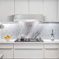 a kitchen with white cabinets and marble counter tops, along with an oven hood over the stove