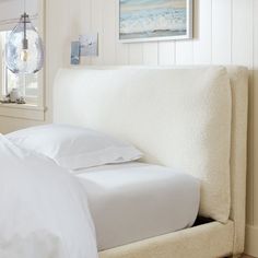 a bed with white sheets and pillows on top of it next to a wall mounted light