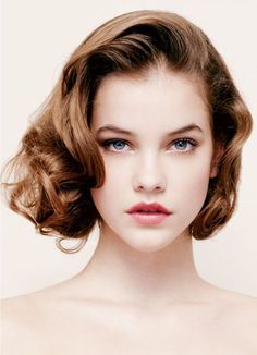 a close up of a woman with blue eyes and curly hair wearing an elegant hairstyle