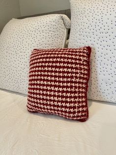 a red and white pillow sitting on top of a bed next to two other pillows