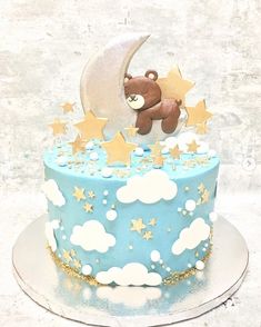 a blue cake with gold stars and a teddy bear sitting on top of the moon