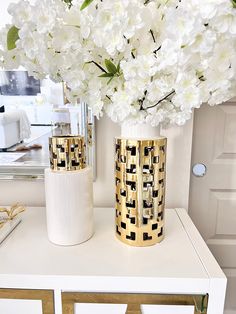 white and gold vases with flowers in them on a table next to a mirror