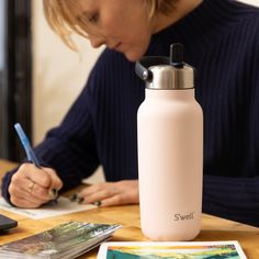 a woman writing on a piece of paper while sitting at a table with a water bottle