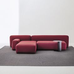 a large red couch sitting on top of a gray rug next to a white wall