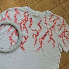 a t - shirt with red lightning bolts on it and a circular object laying on the floor