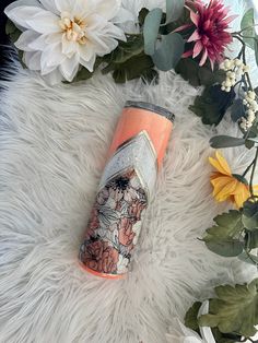 an orange and pink tumbler sitting on top of a white fur covered floor next to flowers