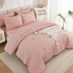 a bed with pink comforter and pillows in a room next to a white table