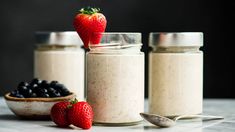 three jars filled with oatmeal sitting on top of a counter next to berries