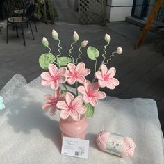 a pink vase filled with flowers sitting on top of a table next to a ball of yarn