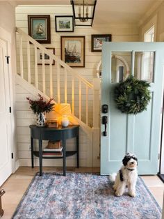 a dog sitting in front of a blue door on a rug next to a table