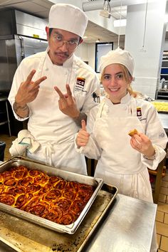 two chefs posing for the camera in front of a large pan of food that has been cooked