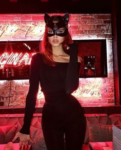 a woman wearing a cat mask standing in front of a neon sign