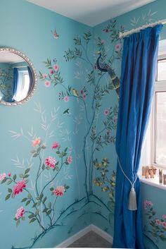 a blue room with flowers painted on the wall and a round mirror hanging above it