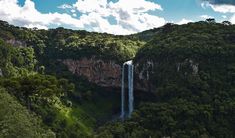 an aerial view of a waterfall in the middle of some trees and mountains with clouds above it