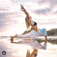 a woman doing yoga on the beach with her hands in the air and one leg up