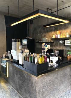 a counter with bottles and glasses on it in a room that has concrete walls, black ceilinging and shelves