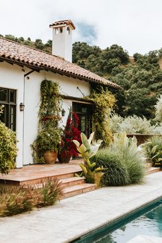 a house with a pool in front of it and lots of plants on the steps