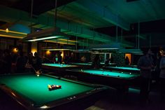 a group of people playing pool in a dark room with green felt balls on the table