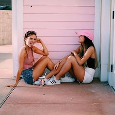 two women sitting on the ground next to a pink wall