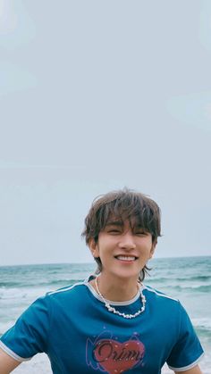 a young man standing on top of a sandy beach next to the ocean wearing a blue shirt