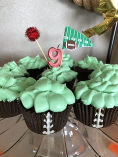 two cupcakes with green frosting and football decorations on top, one has a number 9