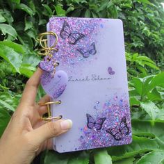 a hand holding a purple notebook with butterflies on it