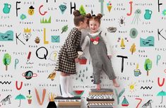 two children standing on top of books in front of a wall with letters and numbers