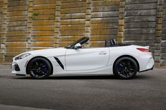 a white bmw z4 roadster parked in front of a brick wall with black rims