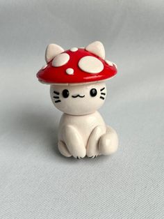 a small white cat with a red mushroom on its head sitting in front of a gray background