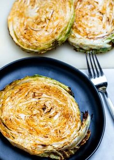 an artichoke on a black plate with silverware next to it and two forks