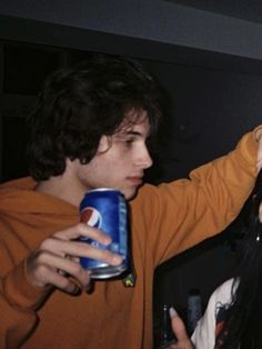 two people standing next to each other and one is holding a can of soda in his hand