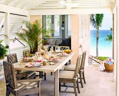 a dining room table with chairs and plates on it near an open door to the beach