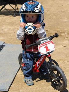 a small child wearing a helmet and riding a bike on the dirt with a number 1 sign in front of him