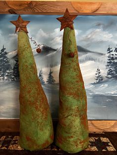 two green christmas trees sitting next to each other in front of a wall with a painting behind them