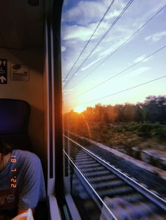 a person sitting on a train looking out the window at the sunset or sunrise with power lines in the background